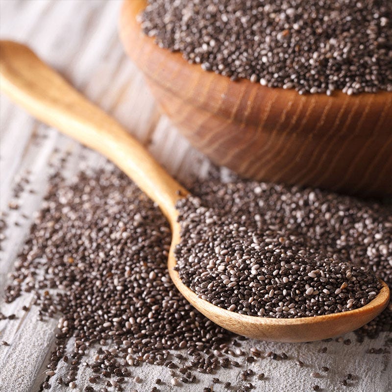 A wooden bowl and wooden spoon holding dried chai seeds